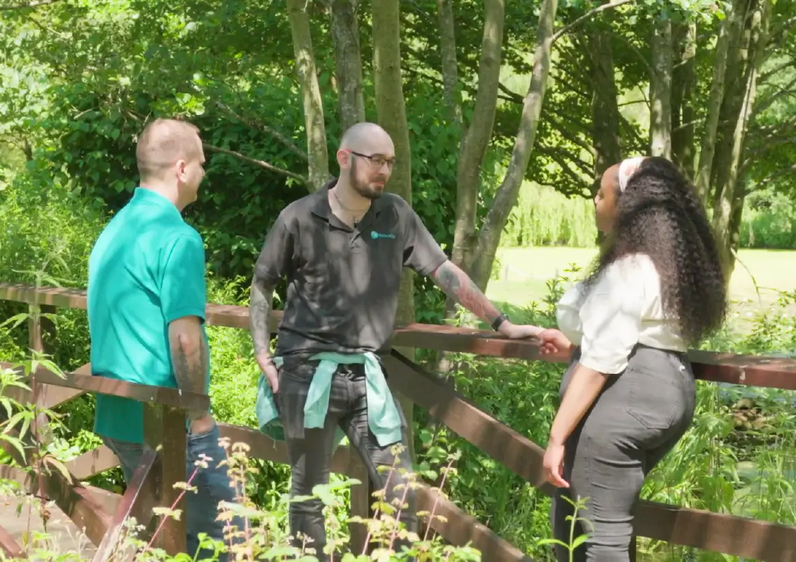Three people talking on a wooden footbridge surrounded by trees